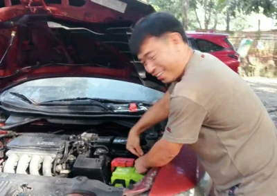 Mechanic completing car battery replacement for a red Honda City at Jet Battery Trading in Rizal.