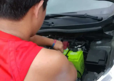 Jet Battery Trading technician installing a green Amaron battery on a red Honda sedan in Rizal.